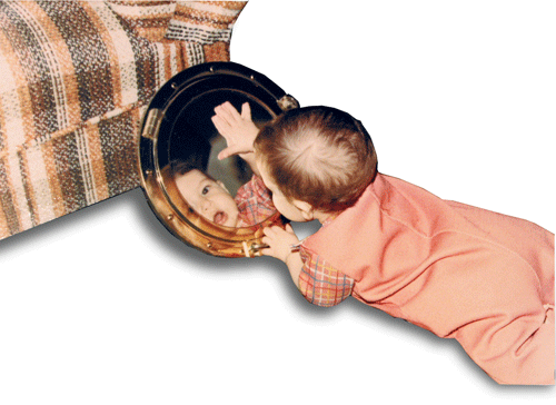 Baby John looking at a mirror by a couch.