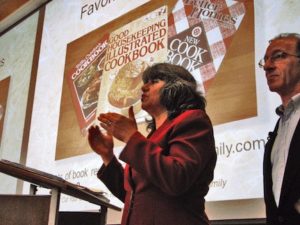 Annette Economides standing in front of a large slide image showing her three favorite cookbooks.
