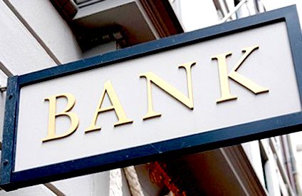 A grey bank sign with golden letters. Some banks will cash peronal checks for a small fee.