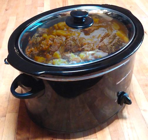 A black crockpot with beef stew in it.