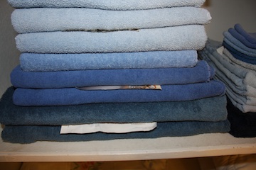 Bed linens stacked on a linen closet shelf.