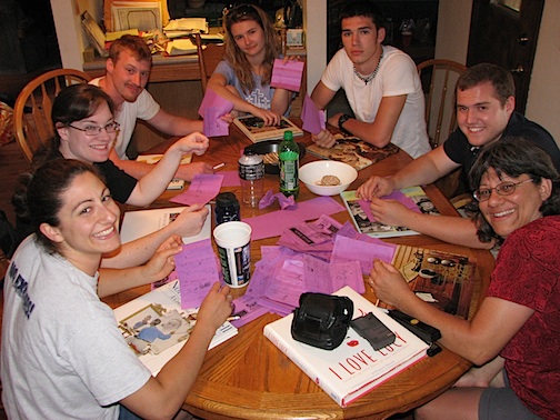 A group of people sitting around a table on game night playing telephone pictionary.