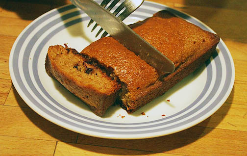 A silver knife and fork being used to cut a loaf of chocolate chip zucchini bread. A delicious snack for kids.