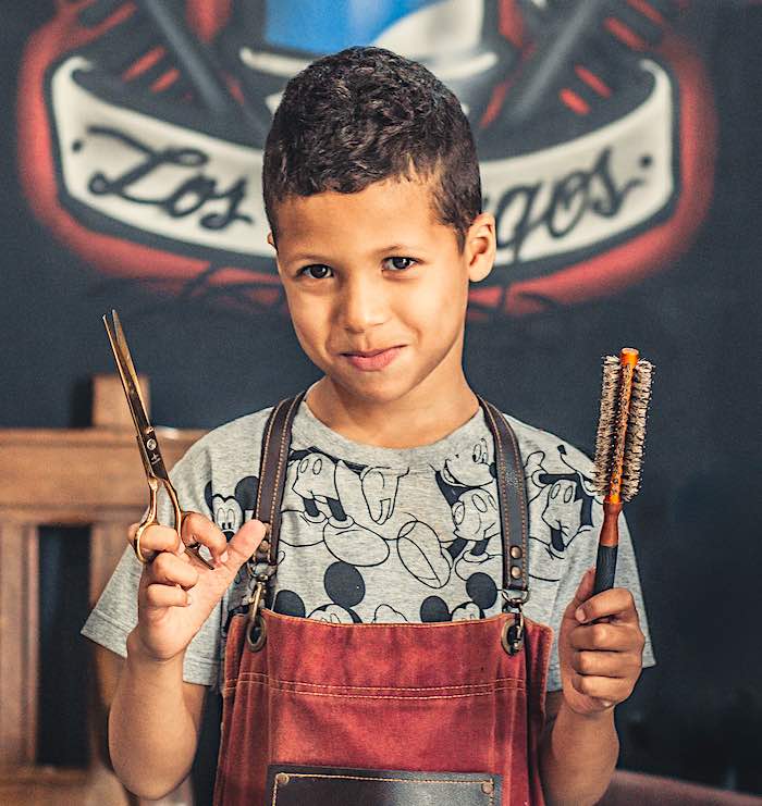 A young boy holding hair cutting scissors and a brush. Ready to give a home hair cut to save money.