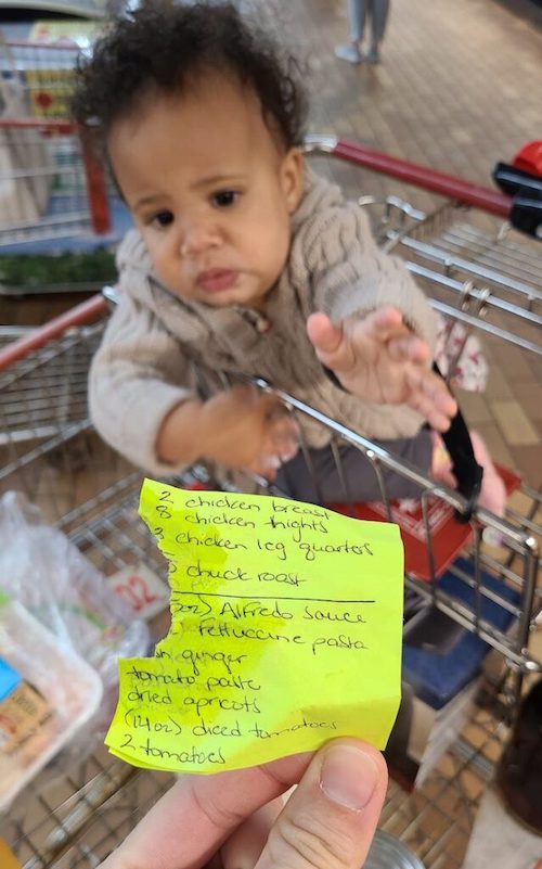a baby in a shopping cart reaching for a shopping list that she chewed.