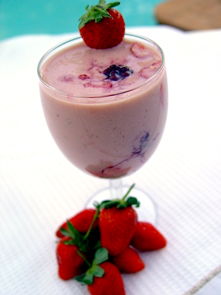 A smoothie in a tall stemmed glass with strawberries on it. A great snack for young children.