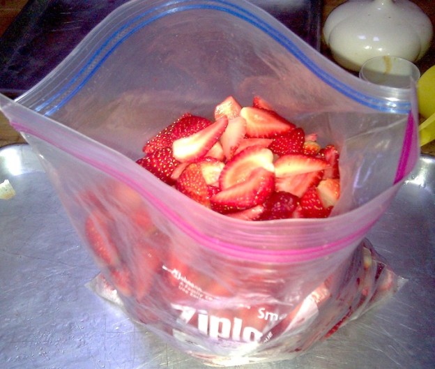 Cut-up frozen strawberries are put into a zippered plastic bag ready to be stored in the freezer.