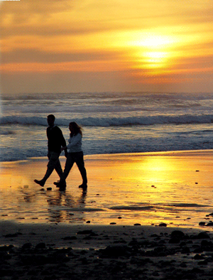 A couple walking on the beach at a timeshare at sunset.