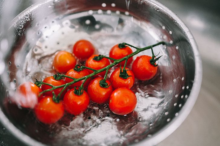 Tomatoes being rinsed in a collander.