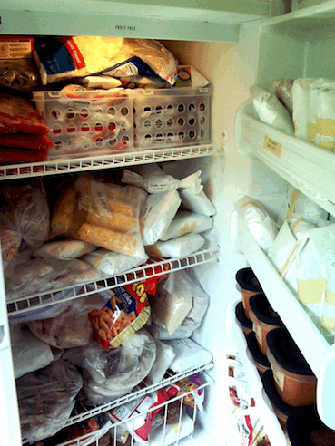 Upright freezer crammed with frozen food - very messy.