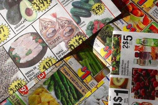 Several grocery ads in a pile on the counter.